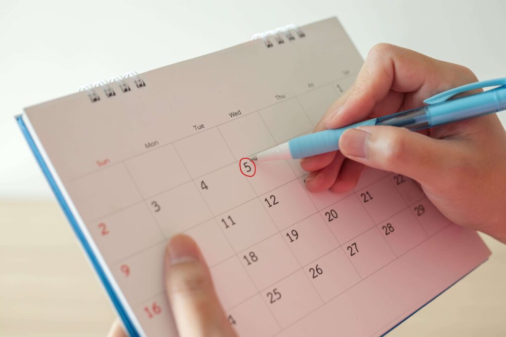 Mano con bolígrafo marca la quinta fecha del calendario con un círculo rojo